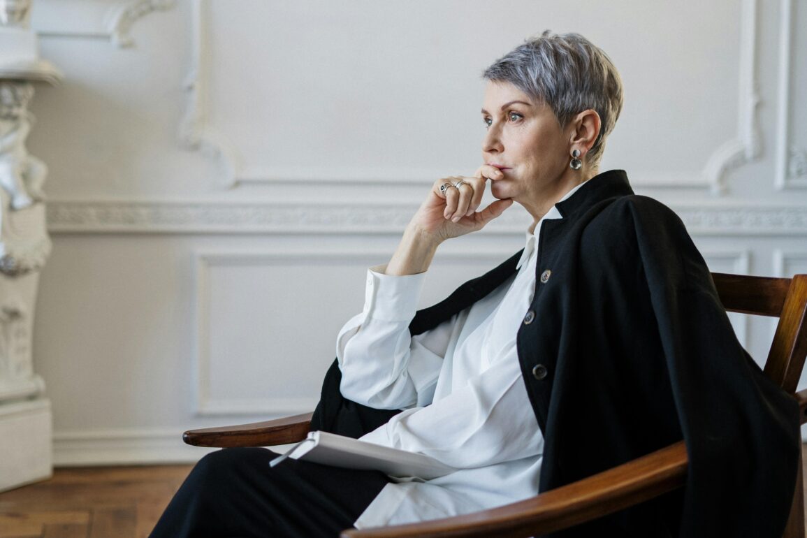 Erfolgreiche Geschäftsfrau mittleren Alters sitzt nachdenklich am Fenster - Sinnfindung für Führungskräfte und Midlife Transition Coaching