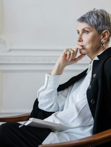 Erfolgreiche Geschäftsfrau mittleren Alters sitzt nachdenklich am Fenster - Sinnfindung für Führungskräfte und Midlife Transition Coaching