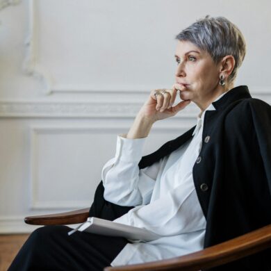 Erfolgreiche Geschäftsfrau mittleren Alters sitzt nachdenklich am Fenster - Sinnfindung für Führungskräfte und Midlife Transition Coaching