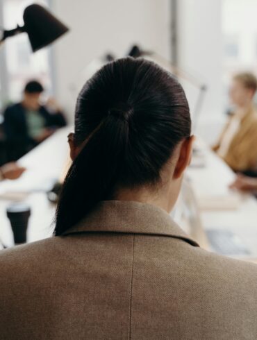 Führungskraft in beigem Blazer sitzt in modernem Büro während Managementmeeting - Unconscious Bias in Führungsentscheidungen vermeiden
